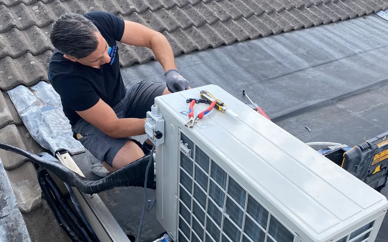 Peter, seen from above, connects the outdoor unit on the roof edge of a house.