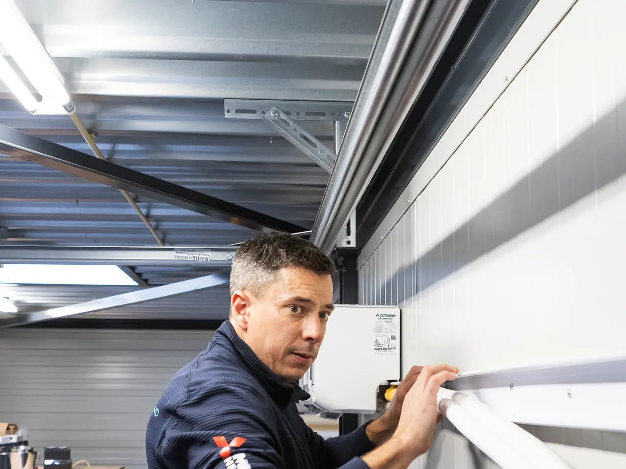 Peter lays the insulated pipe tight along the wall and looks over his shoulder at the camera.