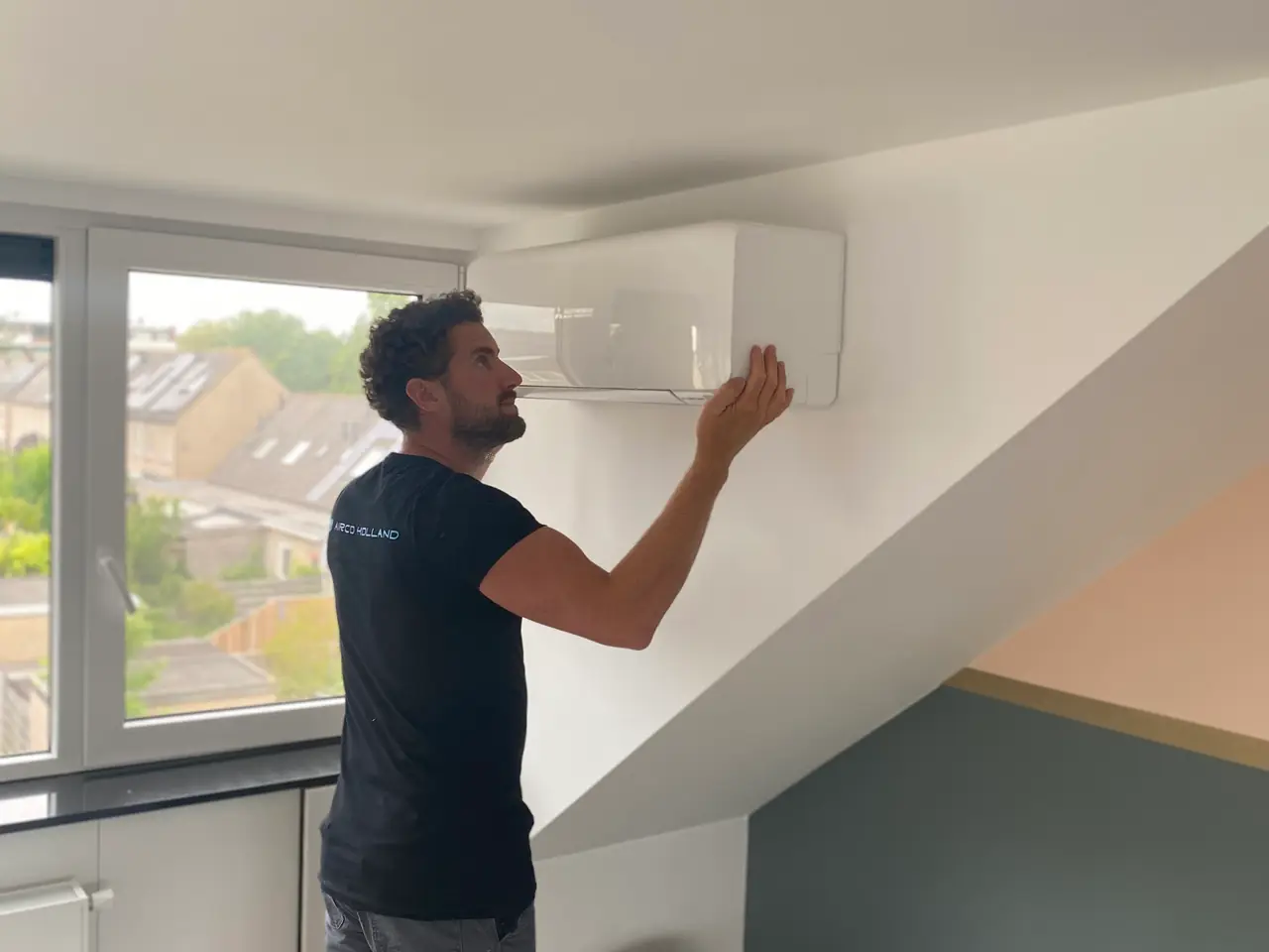 Rein adjusts the louvre of a new white wall unit in an attic room with a view over the roofs.