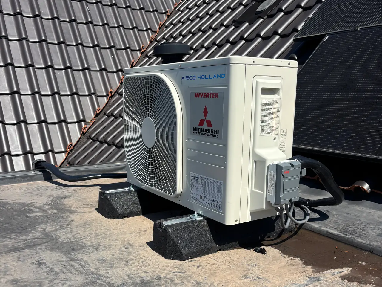 A new outdoor unit on rubber feet on a flat roof, with a dark tiled roof and blue sky.