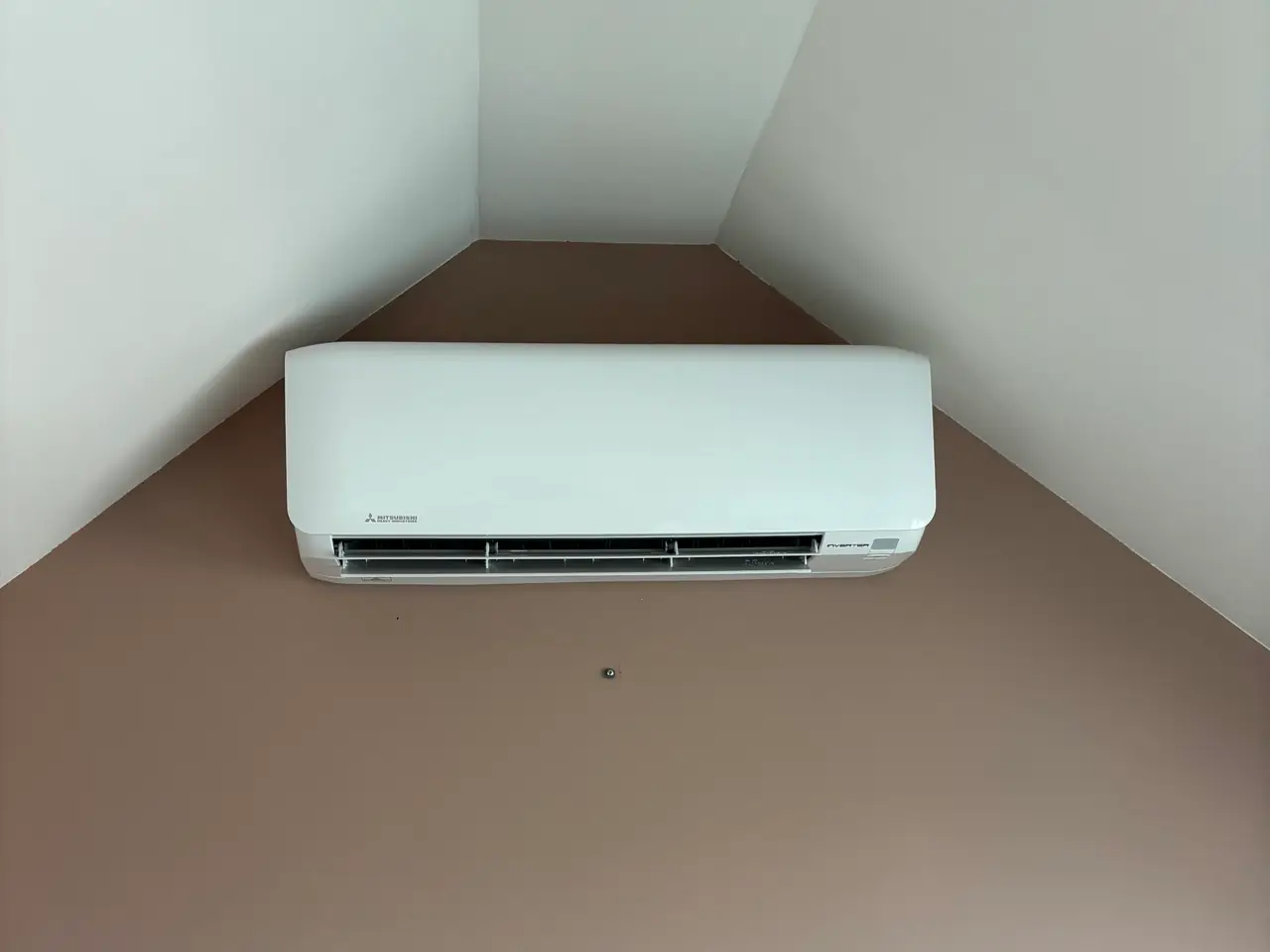 A white wall unit high in the gable of a quiet attic room.