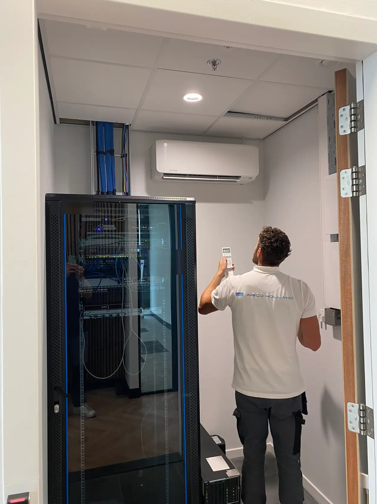 Rein stelt met de afstandsbediening een wit wandmodel in, boven een serverkast in een serverruimte.