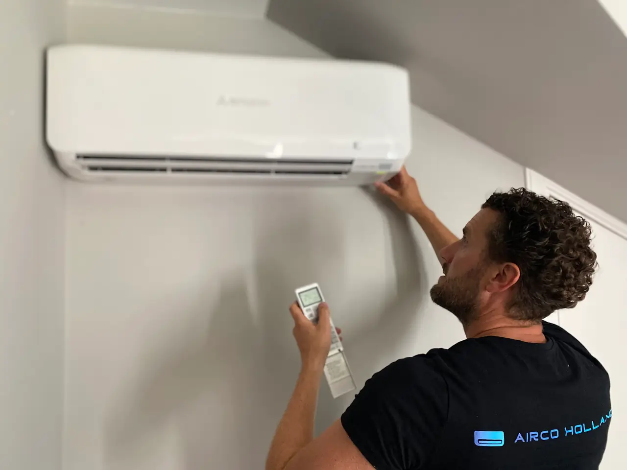 Rein bekijkt een wit wandmodel aan de muur, met de afstandsbediening in zijn hand.
