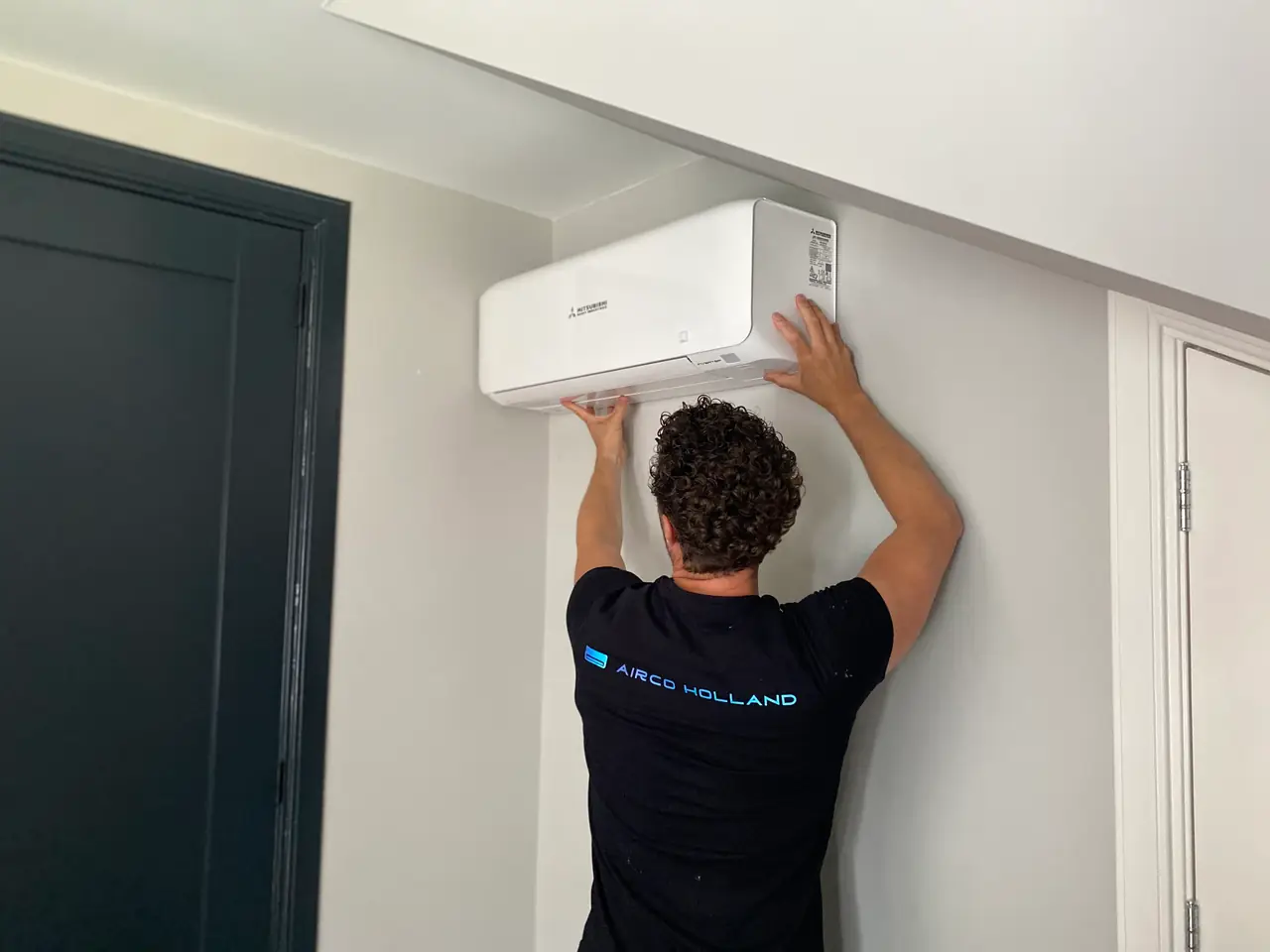 Rein hangt met beide handen een nieuw wit wandmodel op, naast een donkere deur.