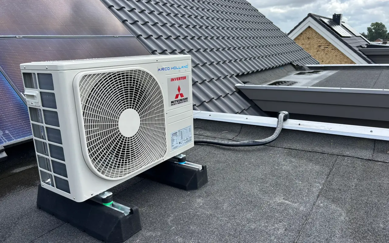 Een nieuwe buitenunit van Mitsubishi Heavy Industries op een plat dak, naast een pannendak met zonnepanelen.