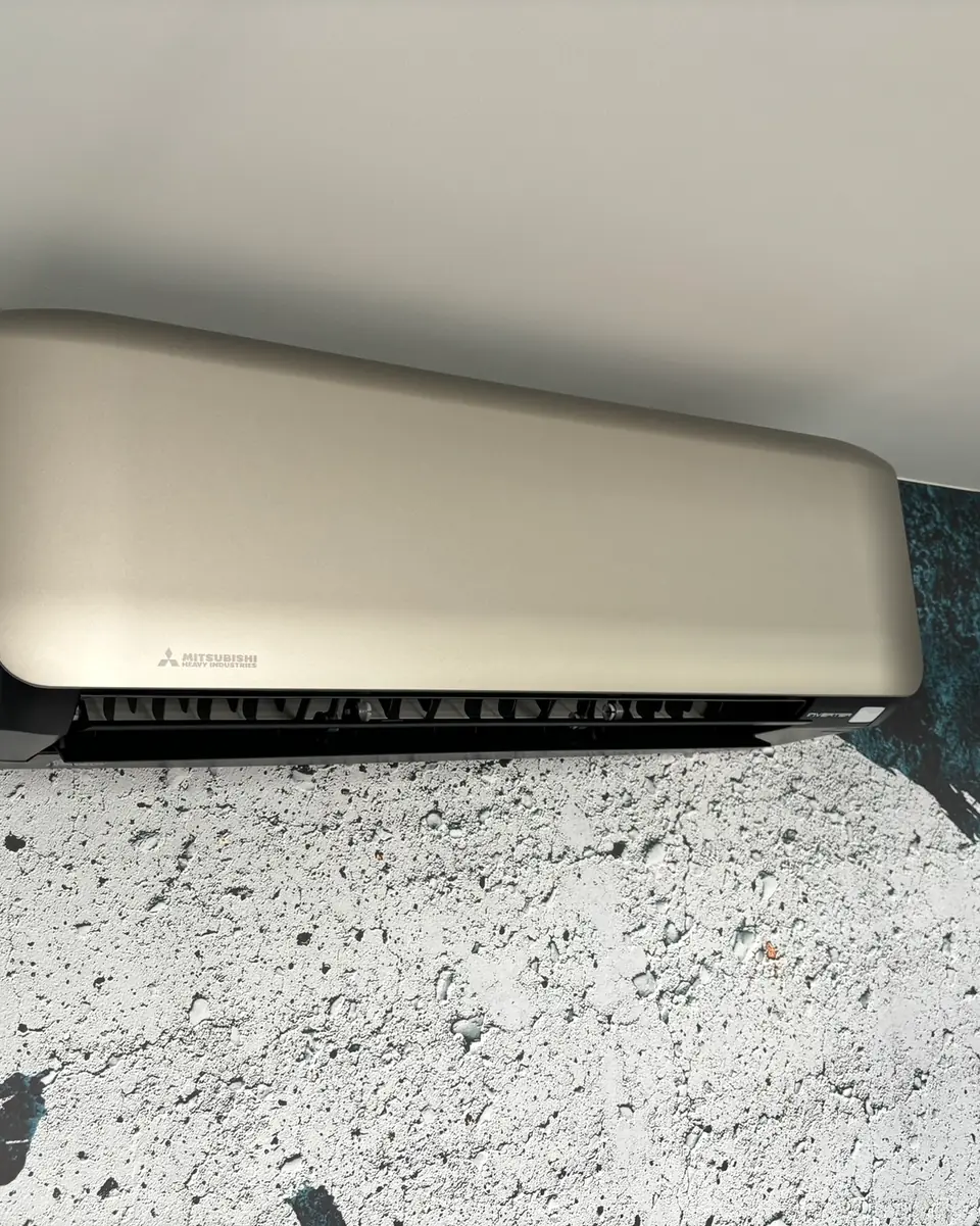 Een champagnekleurig wandmodel van Mitsubishi Heavy Industries, schuin van onderen, tegen gevlekt behang.