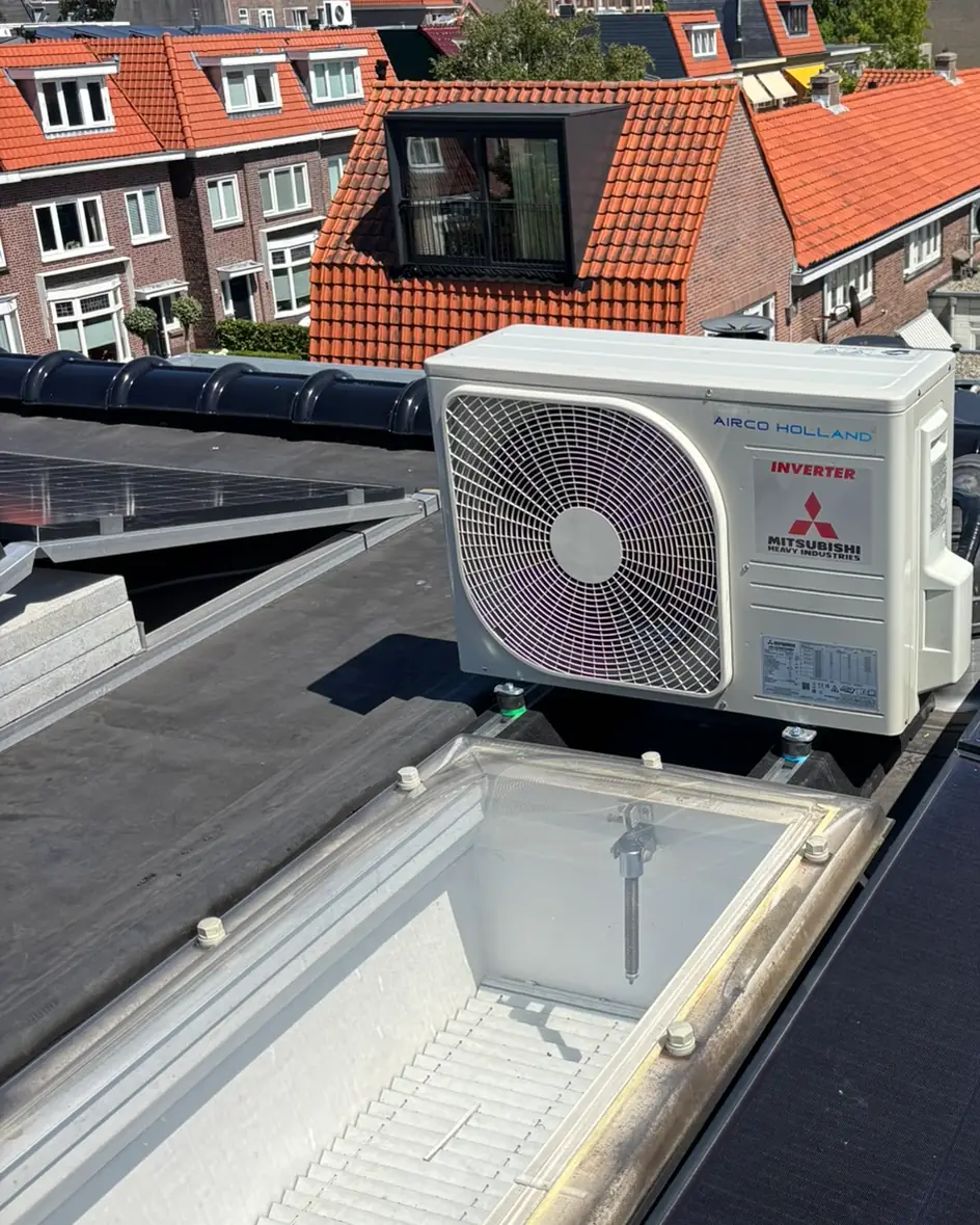 Een buitenunit van Mitsubishi Heavy Industries op een plat dak, met oude pannendaken erachter.