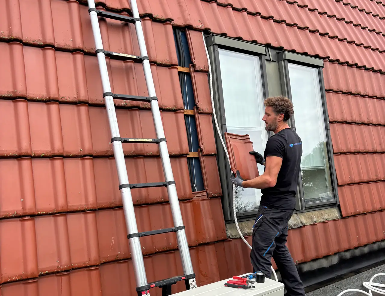 Rein werkt bij het raam in een rode pannengevel; de witte leiding loopt naar de buitenunit vooraan.