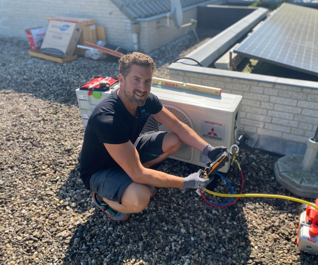 Rein zit op het grind naast een nieuwe buitenunit en lacht in de camera.