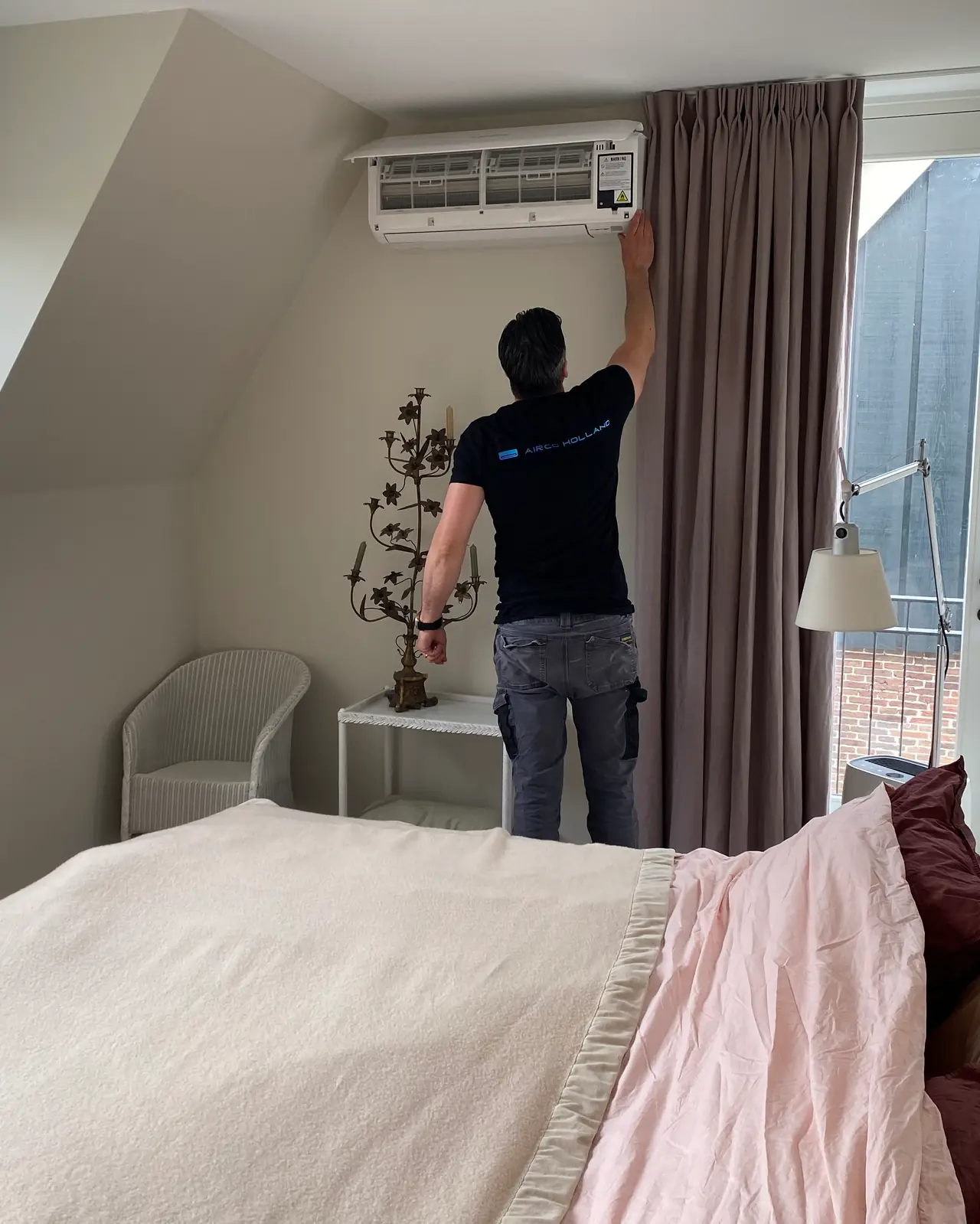 Een slaapkamer onder een schuin dak met het bed op de voorgrond, en Peter achterin bij het wandmodel.