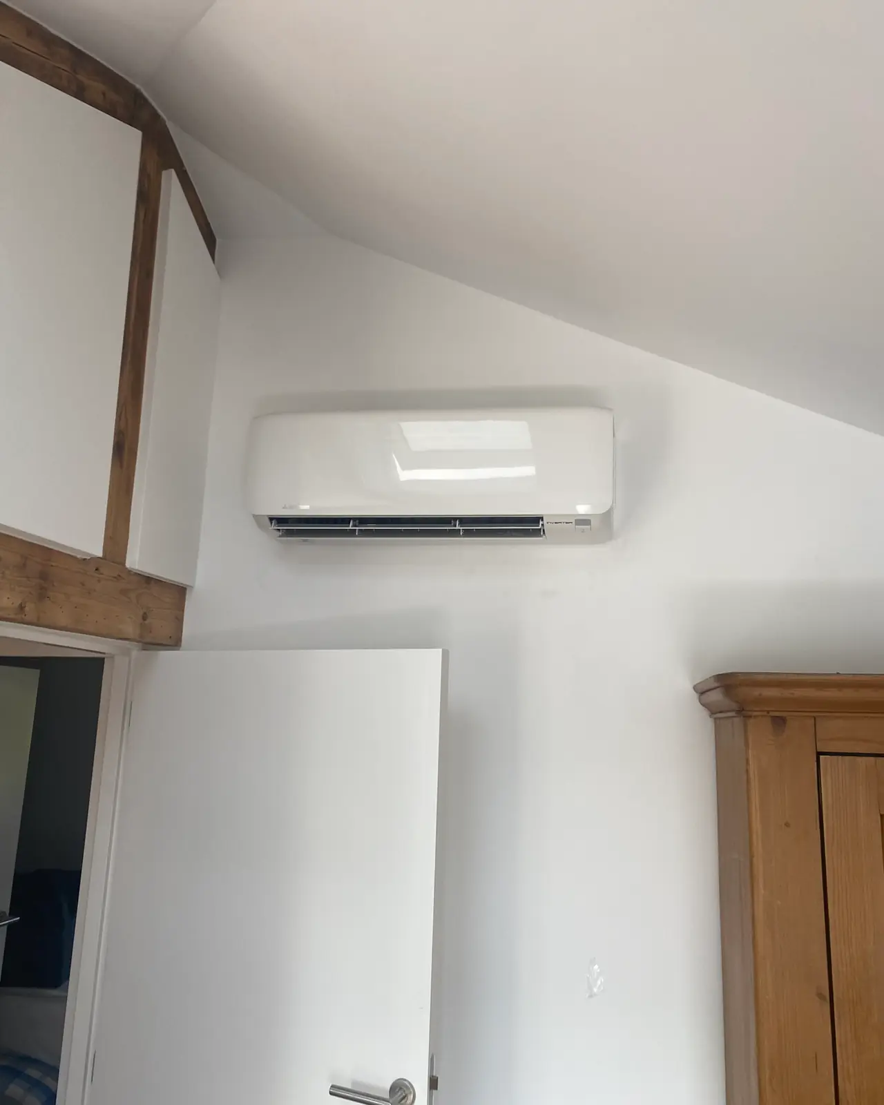 Een wit wandmodel boven de deur van een zolderkamer met een houten balk.
