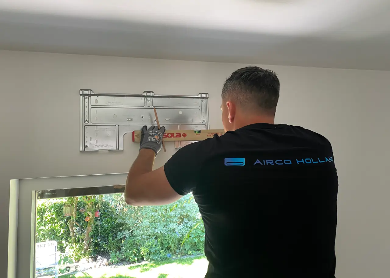 Peter van Airco Holland tekent met een waterpas de plek af voor de ophangplaat van een binnendeel, boven een raam.