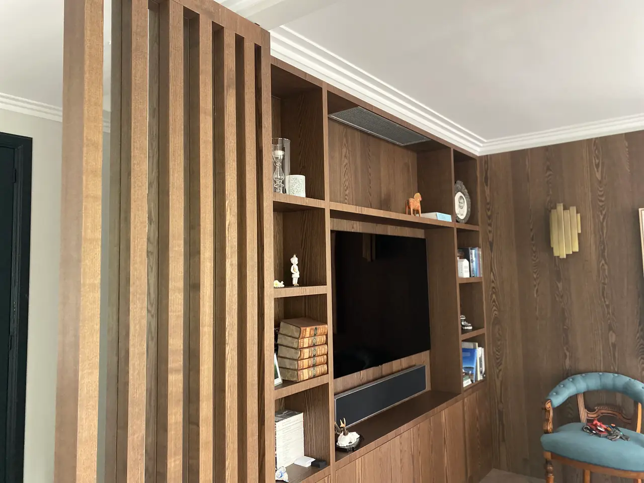 The same living room when it is done: a fitted cabinet with a TV and books, only the grille at the top.