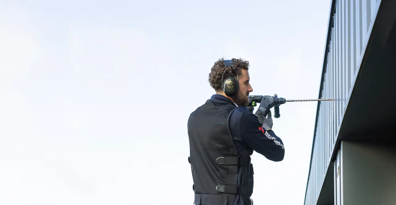 Rein of Airco Holland, wearing ear defenders, drills through a dark wall with a long drill bit.