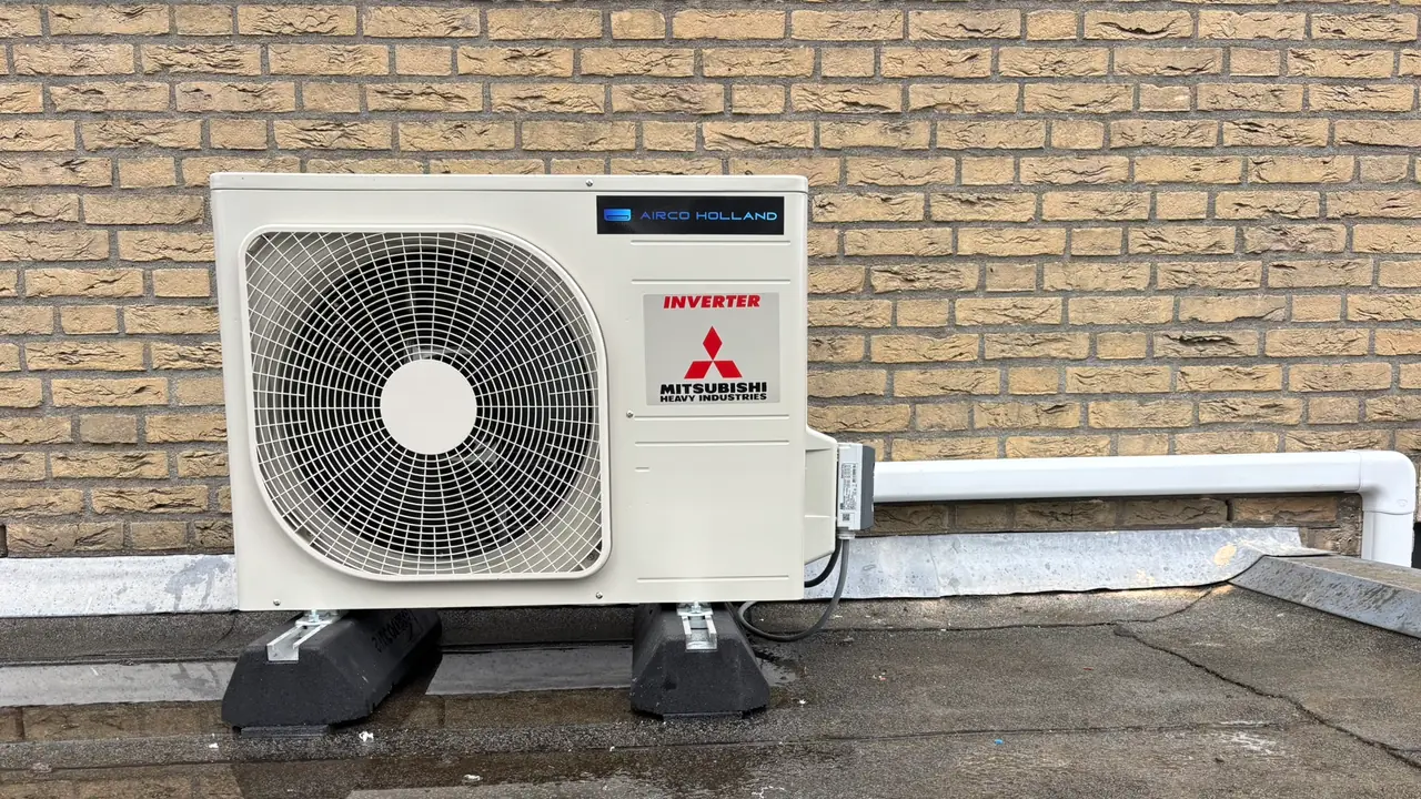 Een buitendeel van Mitsubishi Heavy Industries op dakvoeten tegen gele baksteen, met een plas op het dak.