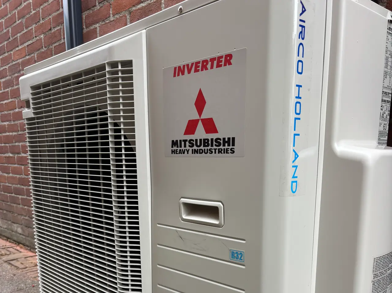 De zijkant van een buitenunit van Mitsubishi Heavy Industries, met Airco Holland in blauwe letters erop.