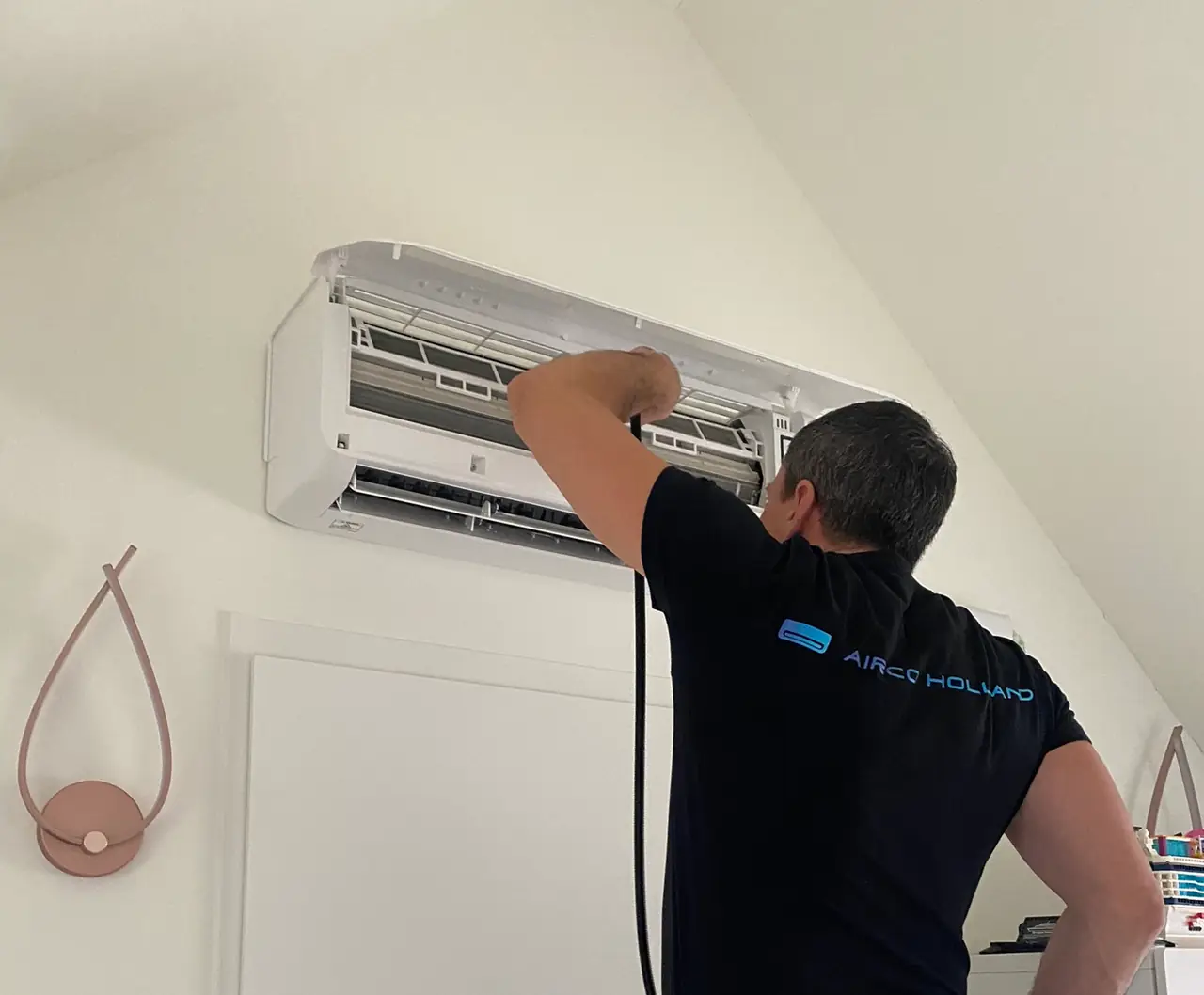 An Airco Holland engineer cleans an opened wall unit with the sprayer.