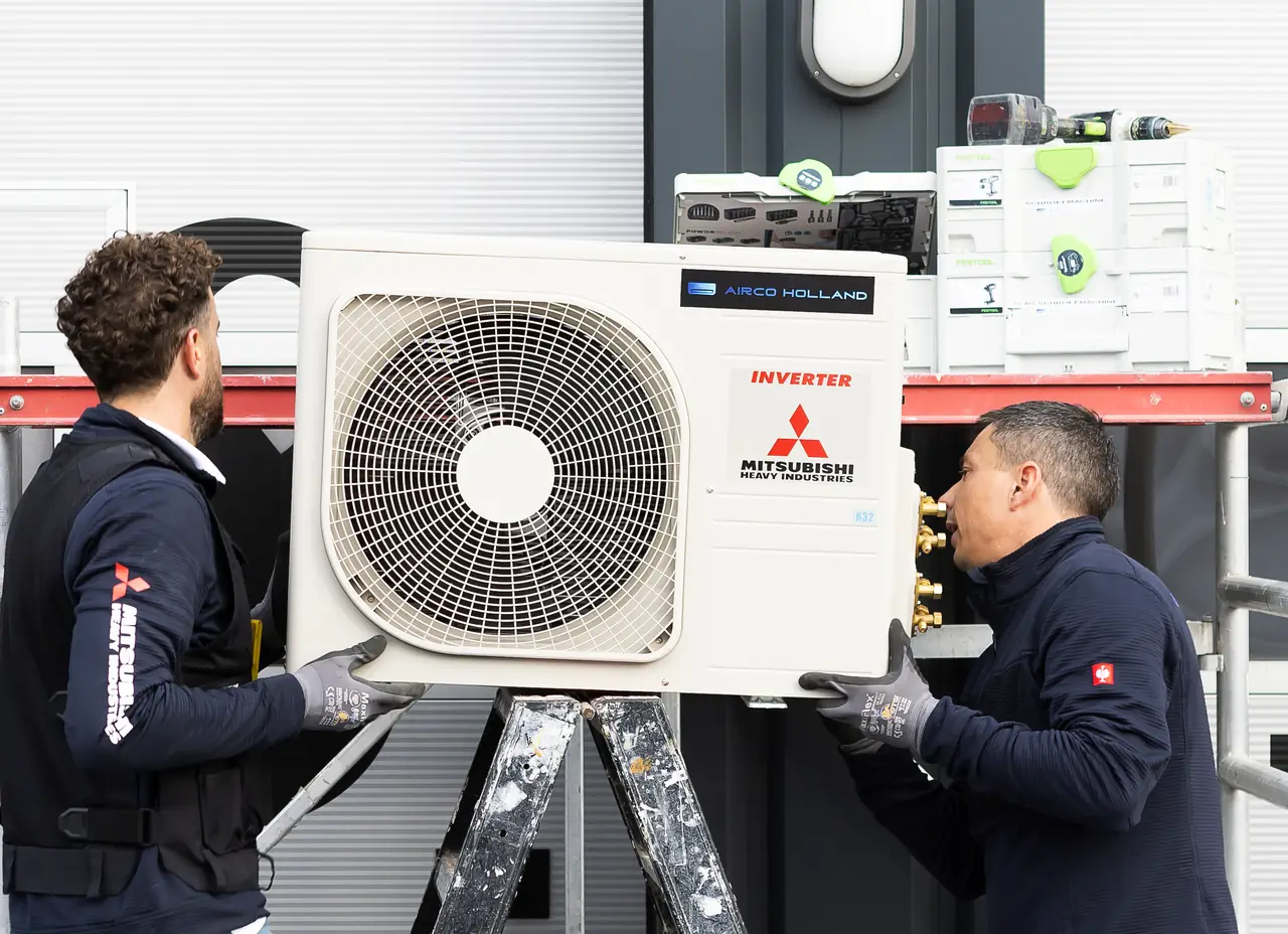 Rein en Peter tillen samen een nieuwe buitenunit van Mitsubishi Heavy Industries op naar de muurbeugel.