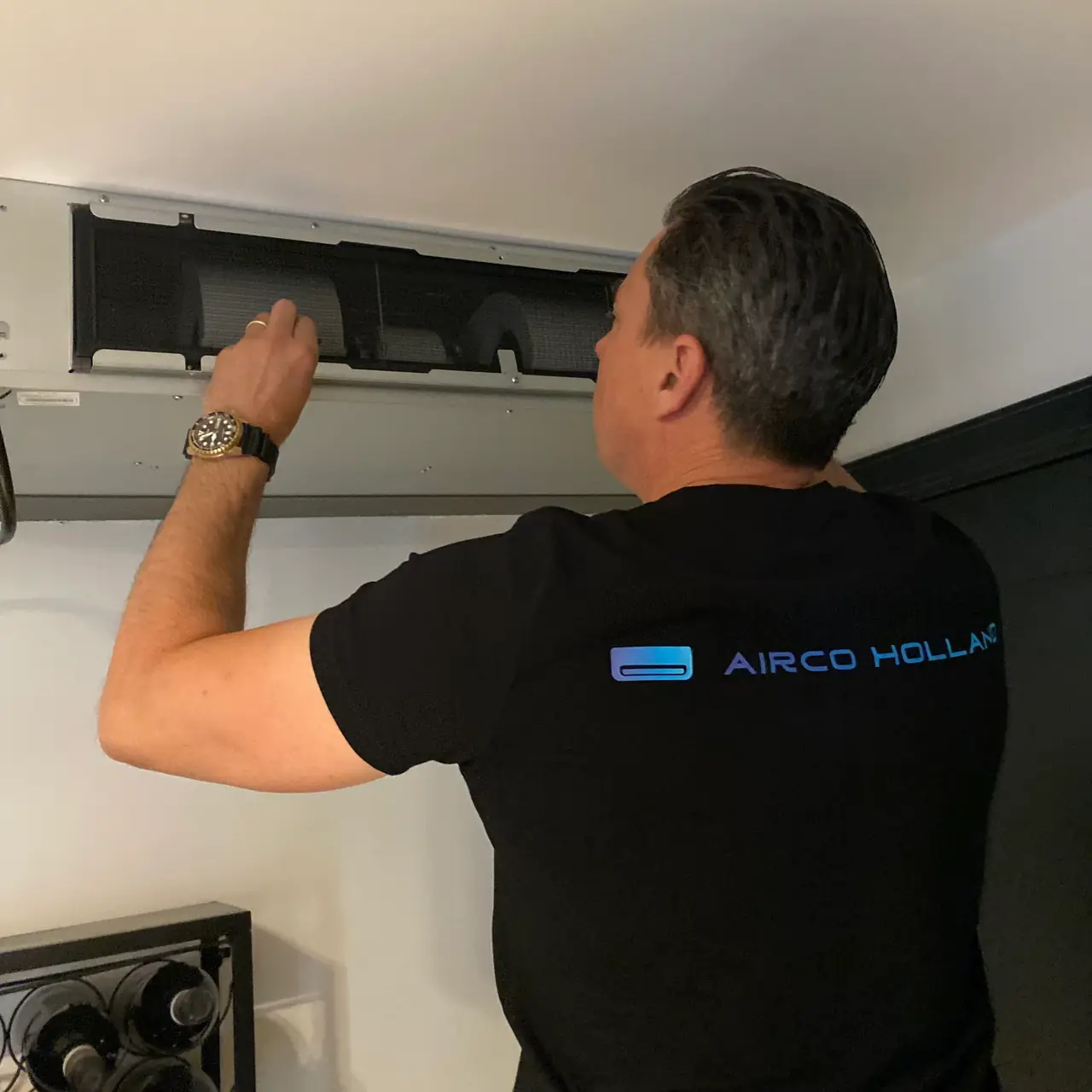 Peter opent het rooster van een airco die in een koof onder het plafond is weggewerkt.